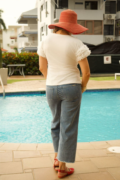 Person wearing a white shirt, blue jeans, and a red hat by a pool.