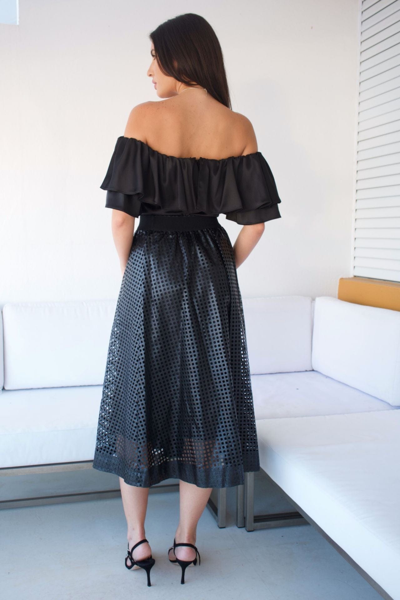 A woman wearing an off-the-shoulder black top with a ruffle detail and silver pants.
