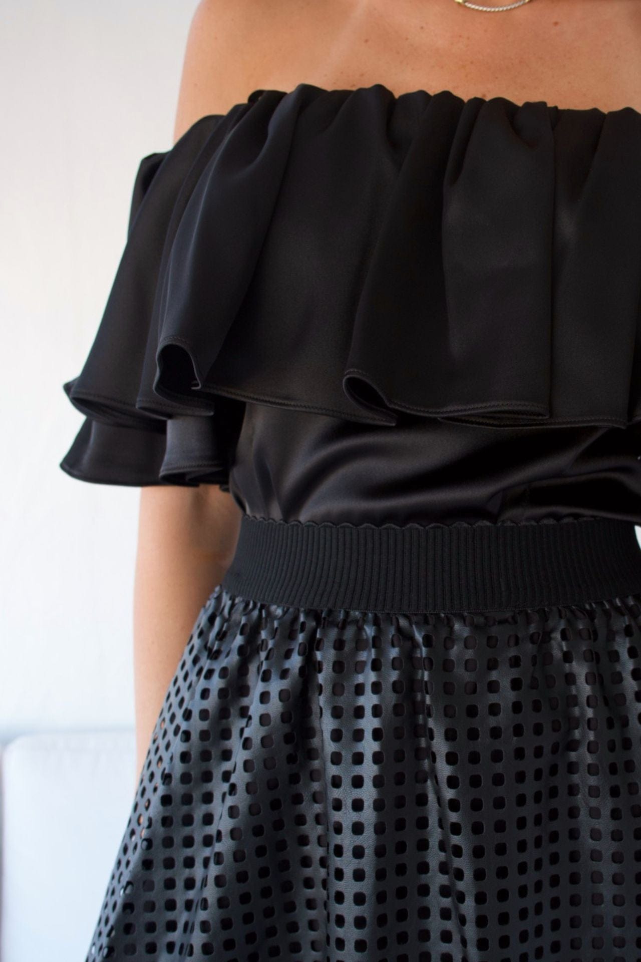 A woman wearing an off-the-shoulder black top with a ruffle detail and silver pants.