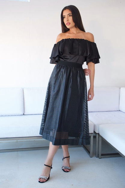 A woman wearing an off-the-shoulder black top with a ruffle detail and silver pants.
