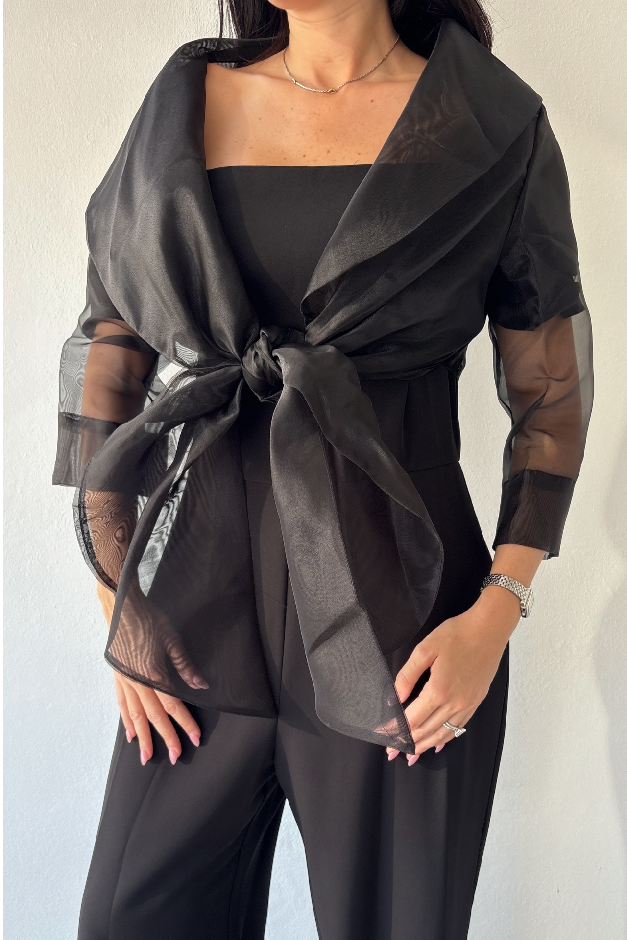 Sheer black organza wrap with three-quarter sleeves and elegant tie-front design over black jumpsuit