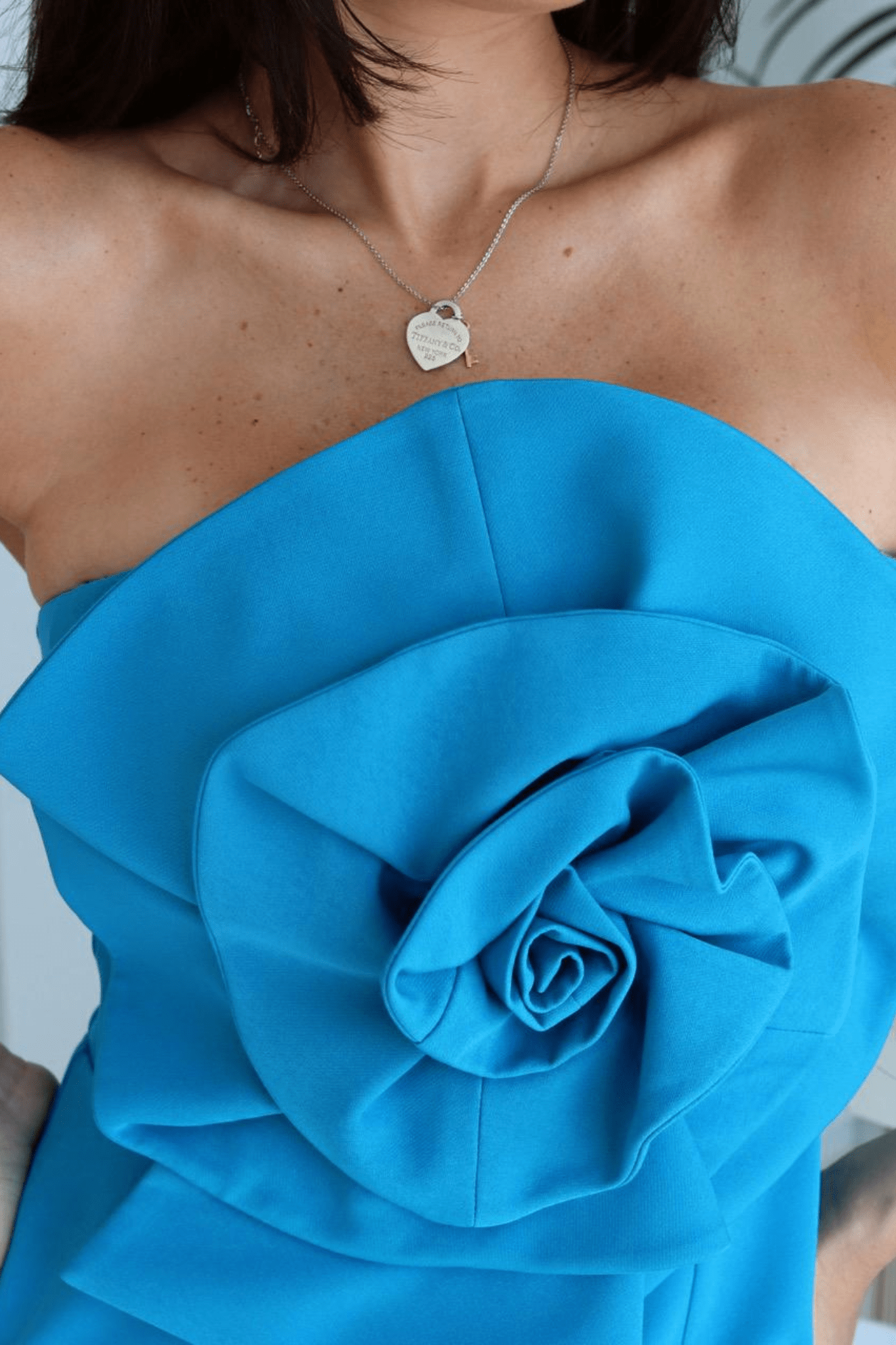 Closeup of a woman wearing a strapless, turquoise cocktail dress with a large flower detail at the front.