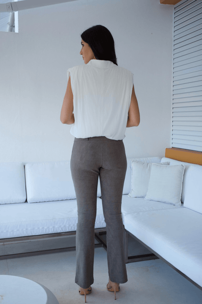 A woman standing in a living room wearing taupe flare pants and a white sleeveless top with a bubble hem.