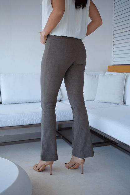 A woman standing in a living room wearing taupe flare pants and a white sleeveless top with a bubble hem.