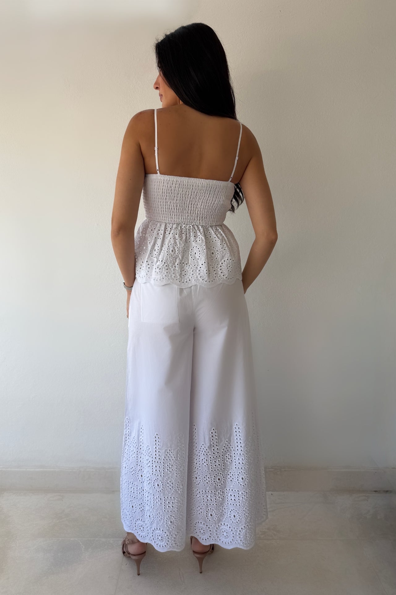 Model wearing the White Coast Eyelet Set featuring a peplum eyelet top with adjustable straps and matching wide-leg pants in white cotton.