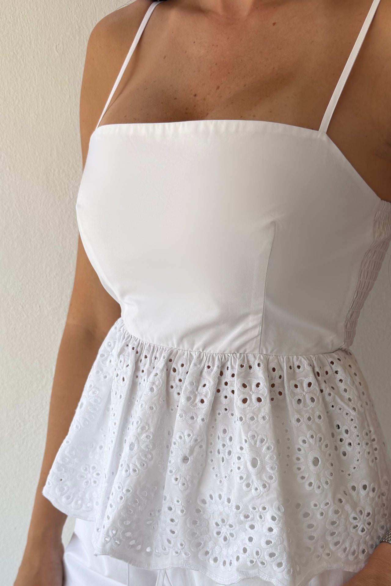Model wearing the White Coast Eyelet Set featuring a peplum eyelet top with adjustable straps and matching wide-leg pants in white cotton.