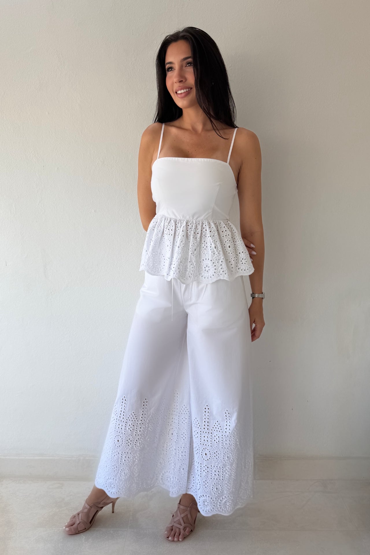 Model wearing the White Coast Eyelet Set featuring a peplum eyelet top with adjustable straps and matching wide-leg pants in white cotton.