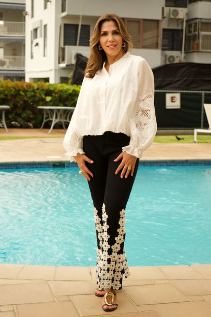 Woman in a white blouse and black pants with floral details standing by a pool.