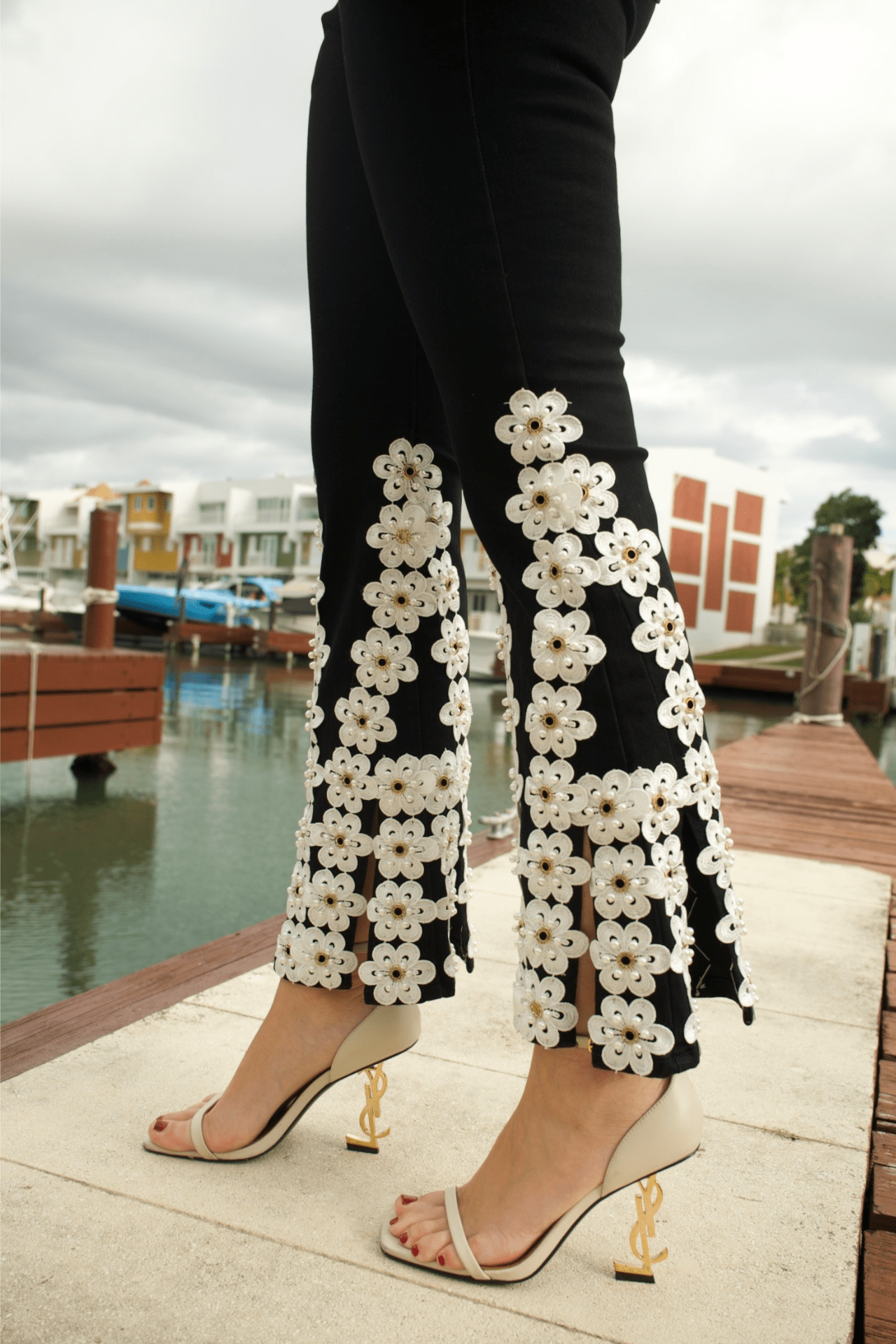 Close-up of white floral embroidery on black denim jeans, showcasing intricate stitching and fine craftsmanship.
