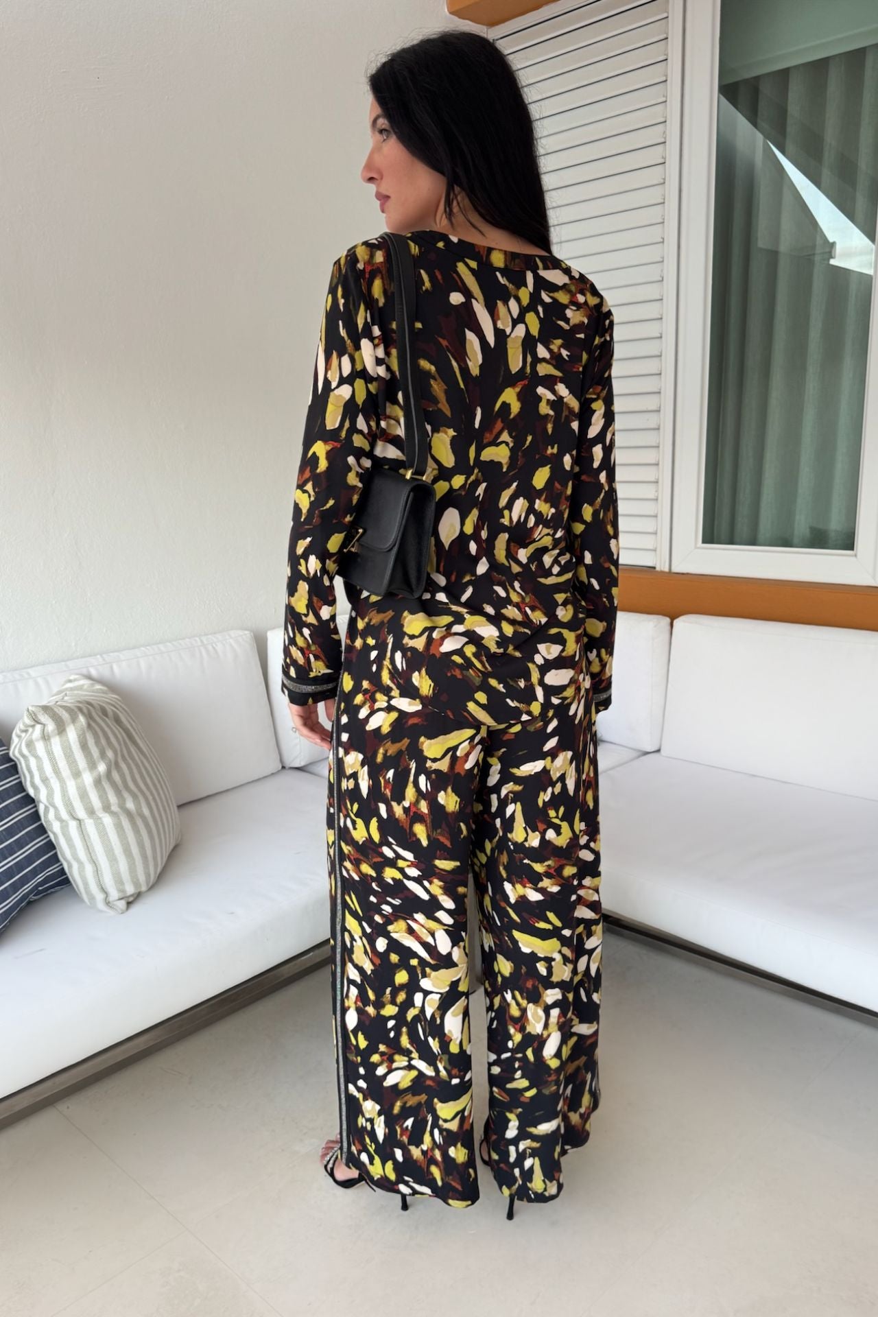 Back view of a woman wearing a satin abstract print tunic and wide-leg pull-on pant set in black and yellow with shimmer trim details