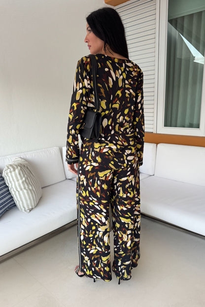 Back view of a woman wearing a satin abstract print tunic and wide-leg pull-on pant set in black and yellow with shimmer trim details