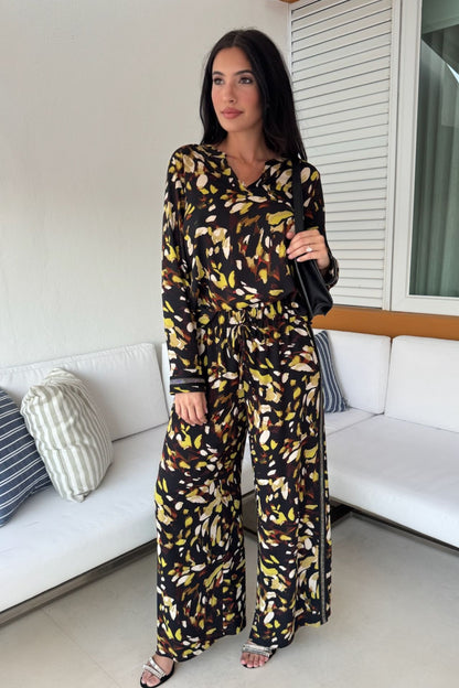 Woman wearing a satin abstract print tunic and wide-leg pull-on pant set in black and yellow with shimmer trim details