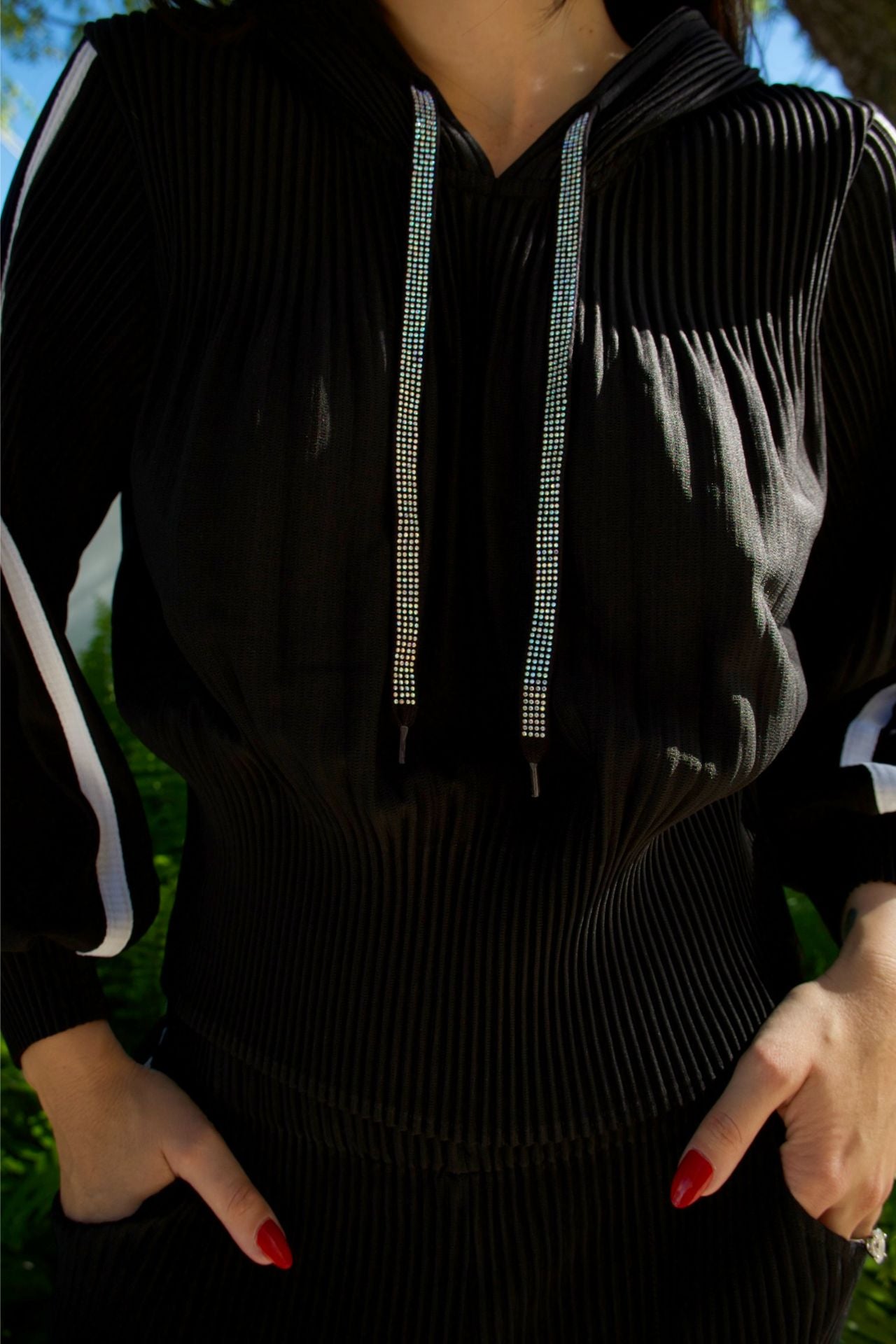 Model wearing black hooded pleated two-piece set with white side stripe and sparkle tie — casual chic outfit Elegance Boutique