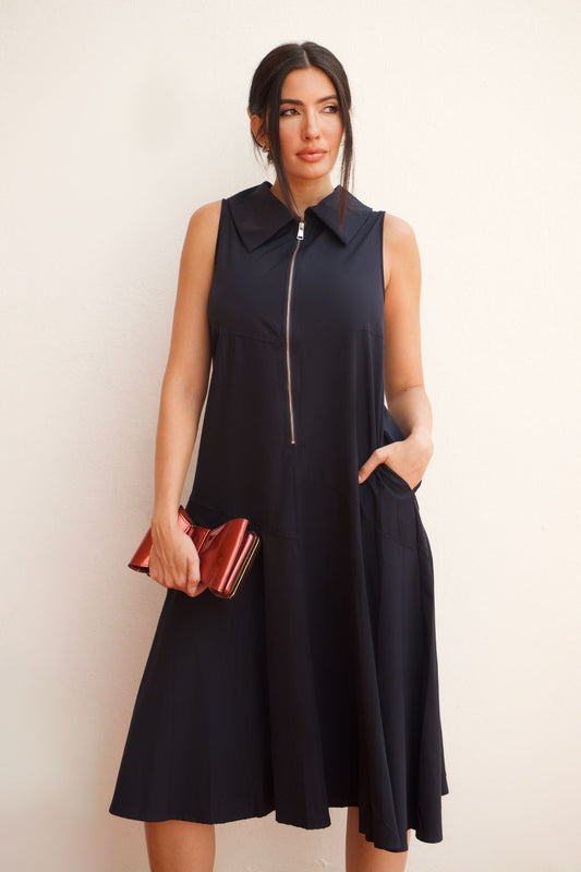 Model wearing a black sleeveless zip-front A-line midi dress with a collar and side pockets, styled with a clutch.