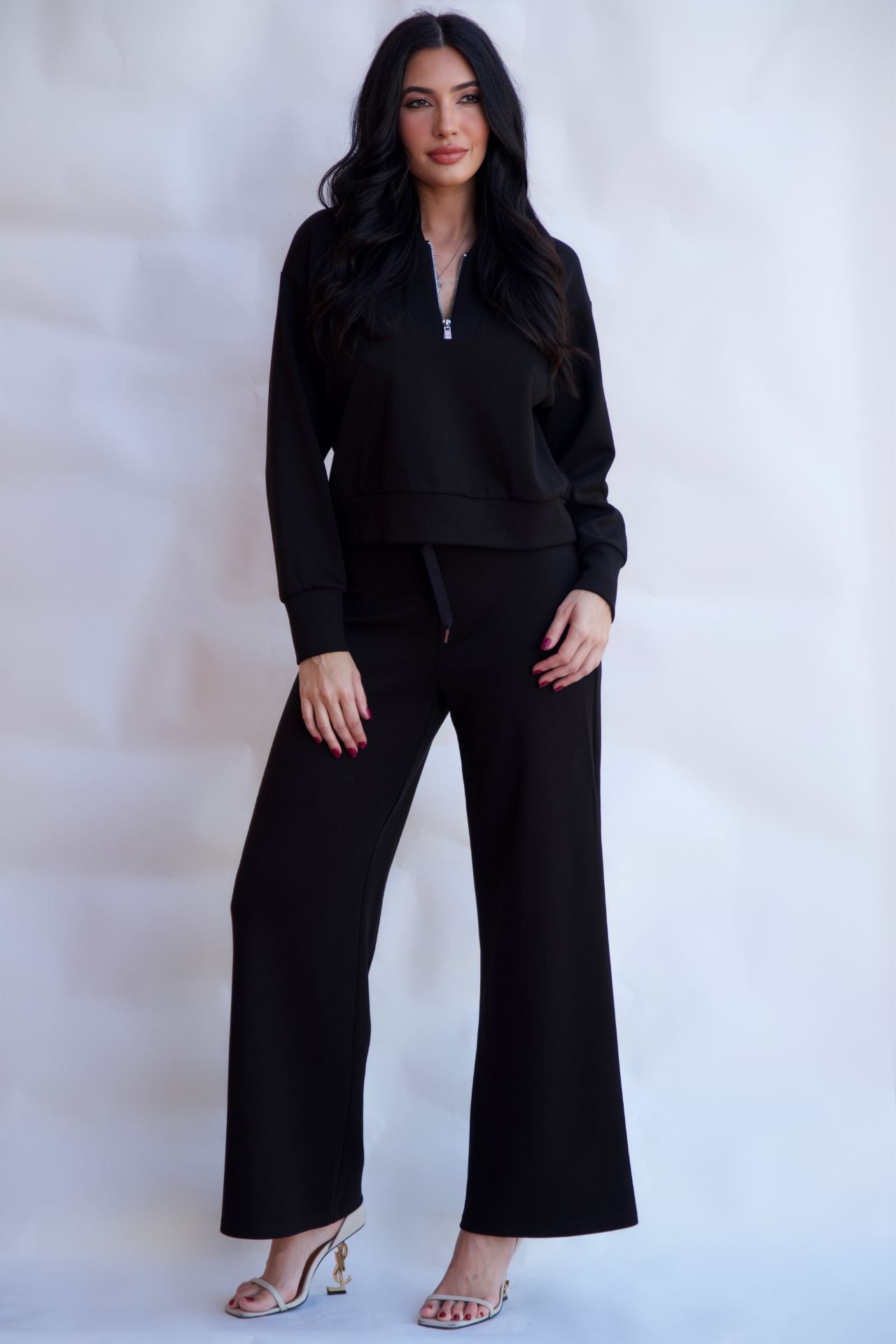 Black sporty chic travel lounge set with zip neck top and wide leg pants styled with heels available online and in-store