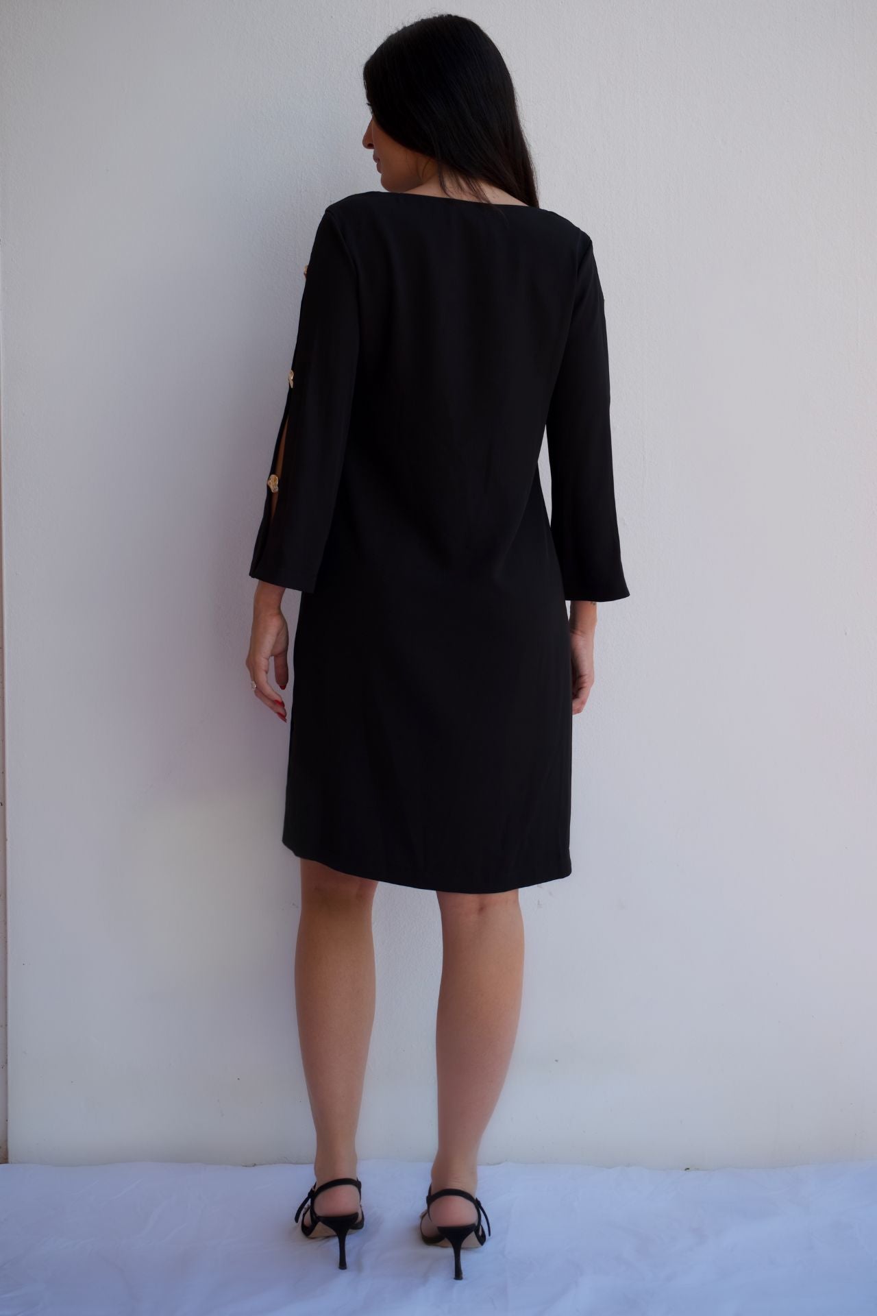 Black V-neck shift dress with gold button sleeve detail, elegant wrinkle-resistant cocktail dress for women, back view.