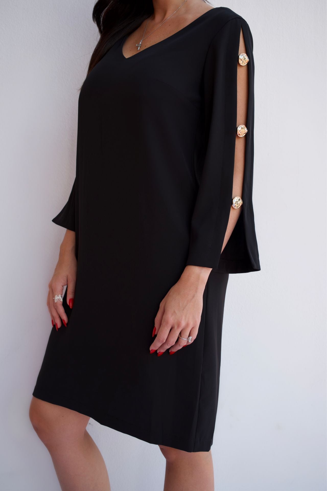 Black V-neck shift dress with gold button sleeve detail, elegant wrinkle-resistant cocktail dress for women, side view.