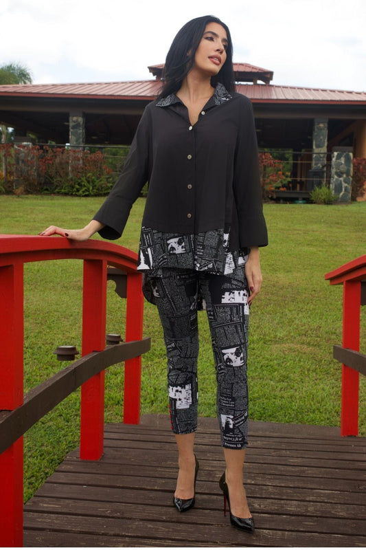 Woman wearing asymmetrical black and white top with newsprint pants and silver chain detail, standing outdoors