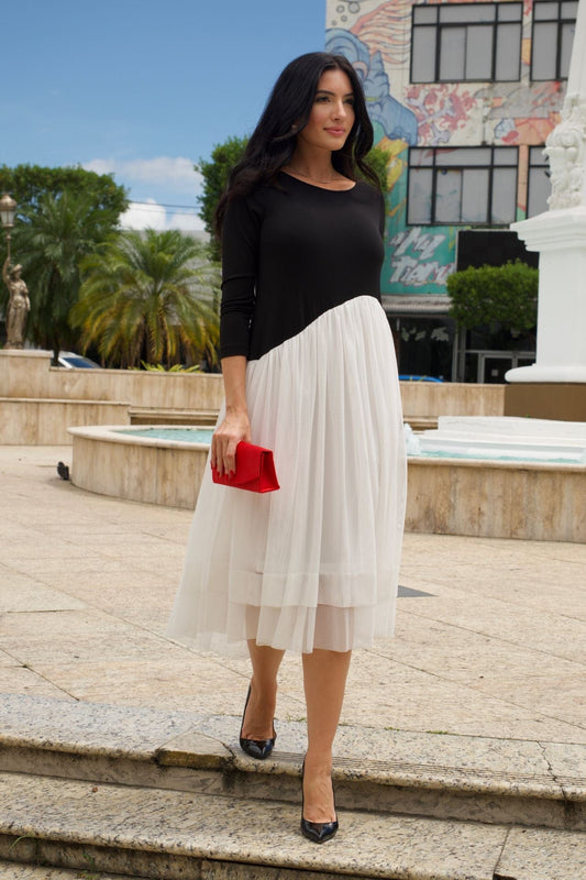 Woman wearing a black and white midi dress with asymmetrical mesh skirt and long sleeves.