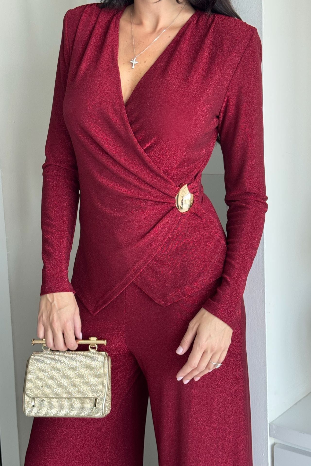 Close up of a woman wearing a burgundy long-sleeve knot-detail wide-leg jumpsuit standing indoors.