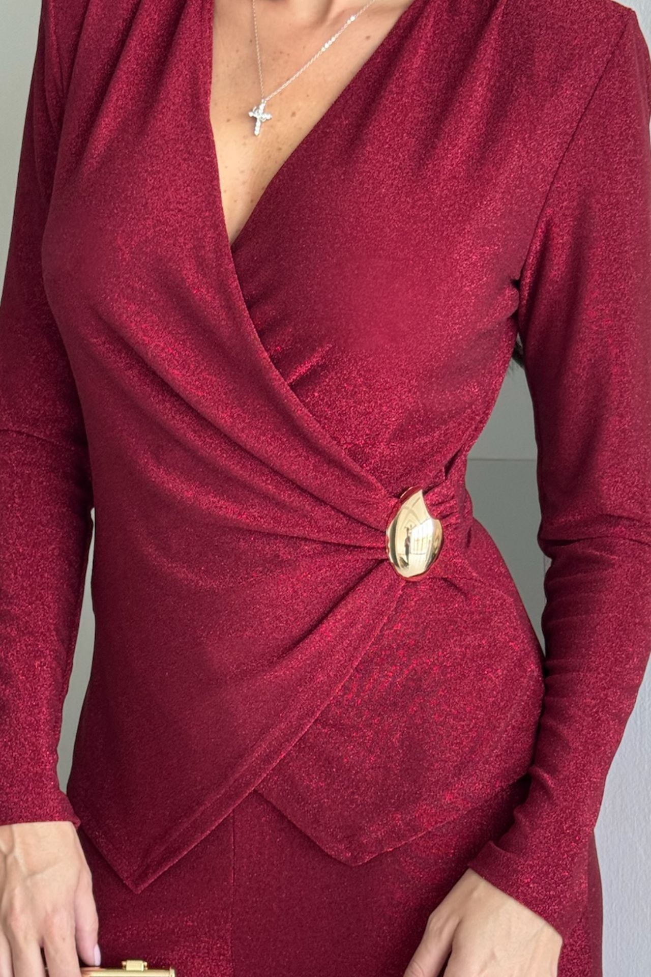 Back view of a woman wearing a burgundy long-sleeve knot-detail wide-leg jumpsuit standing indoors.