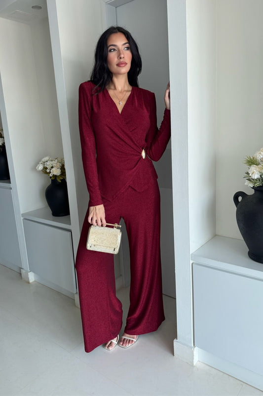 Woman wearing a burgundy long-sleeve knot-detail wide-leg jumpsuit standing indoors.