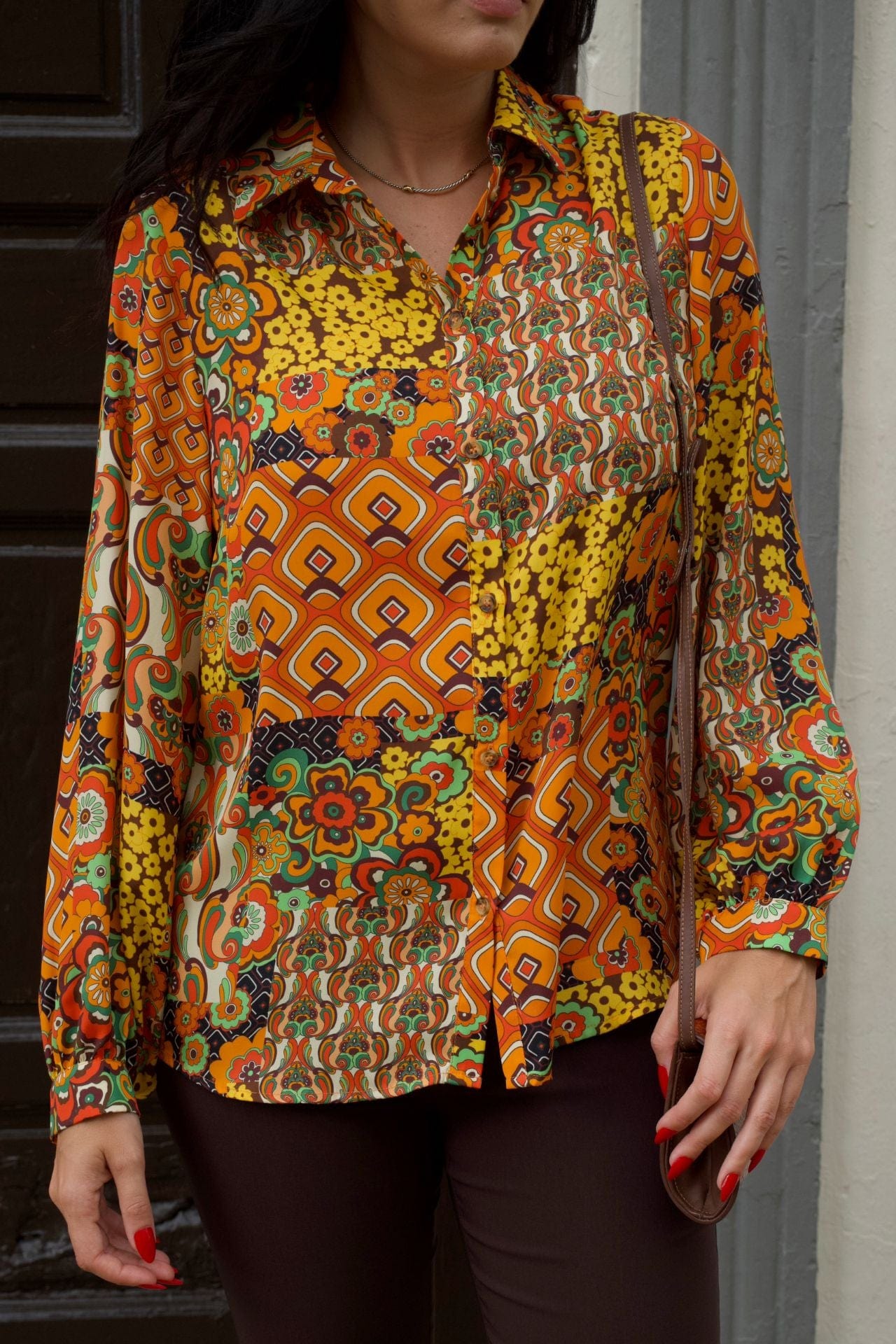 Close up of a woman wearing retro patchwork print blouse with long sleeves and chocolate brown slim pants.