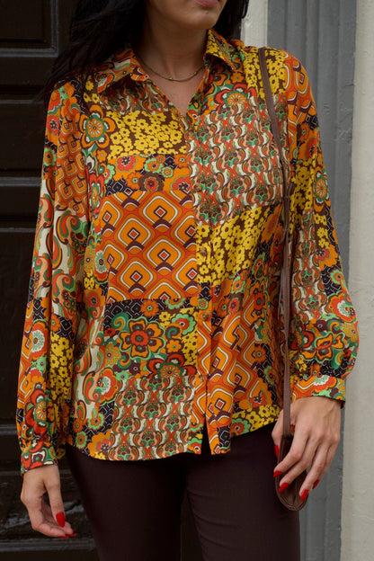 Close up of a woman wearing retro patchwork print blouse with long sleeves and chocolate brown slim pants.