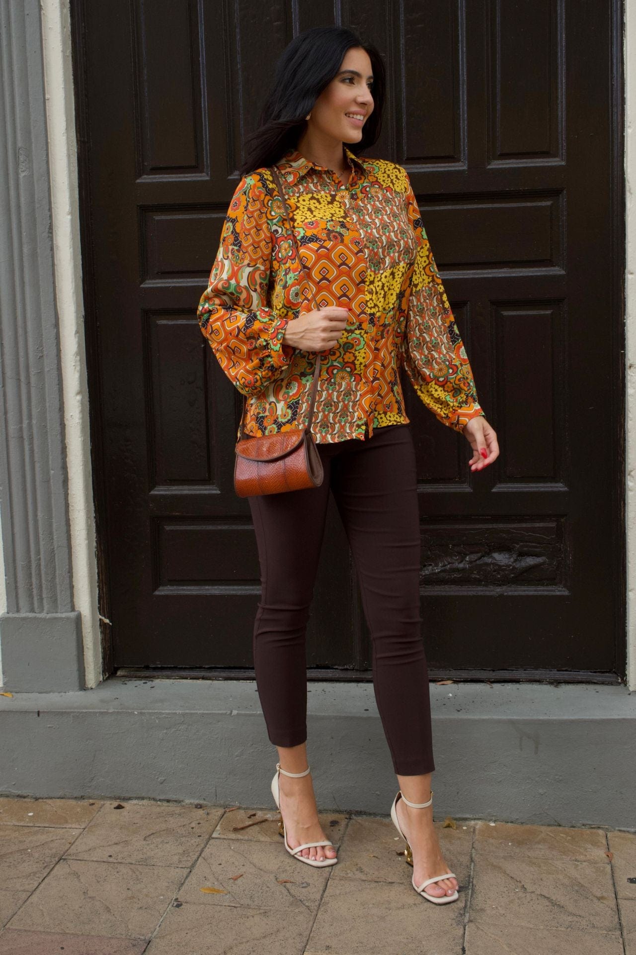 Woman wearing retro patchwork print blouse with long sleeves and chocolate brown slim pants.