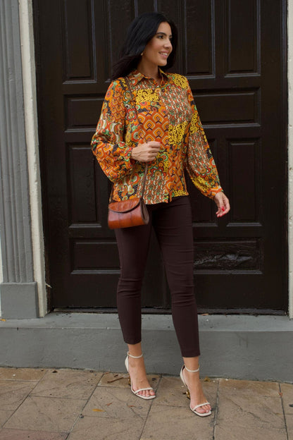 Woman wearing retro patchwork print blouse with long sleeves and chocolate brown slim pants.