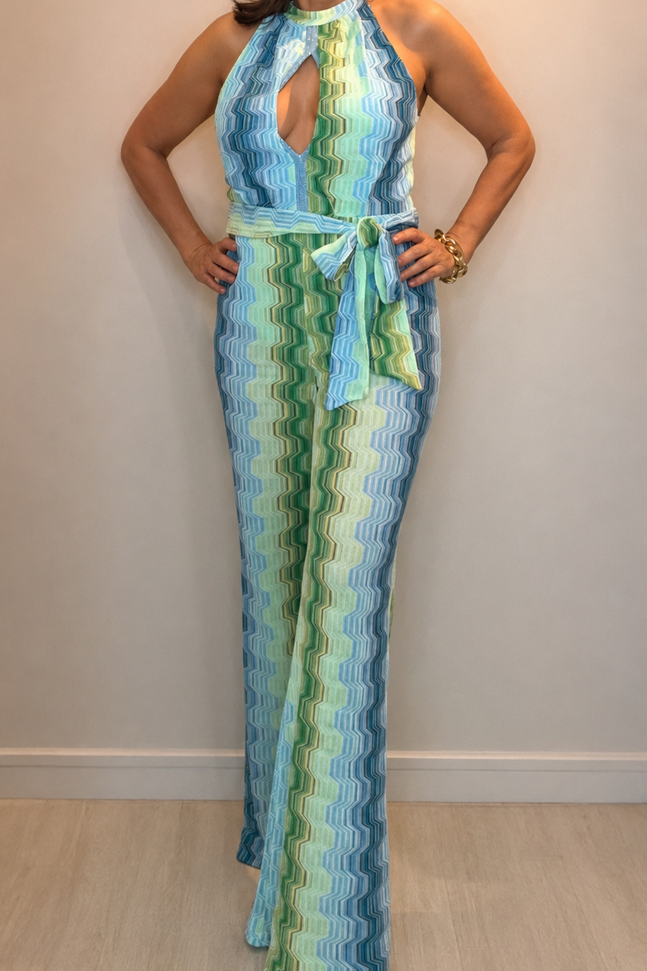 Woman wearing a green and blue wave print halter jumpsuit with waist tie detail and elegant wide-leg silhouette.