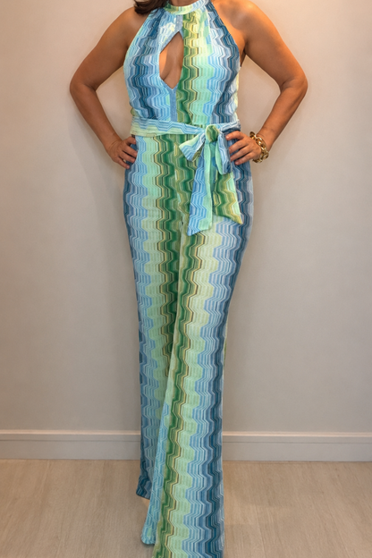Woman wearing a green and blue wave print halter jumpsuit with waist tie detail and elegant wide-leg silhouette.