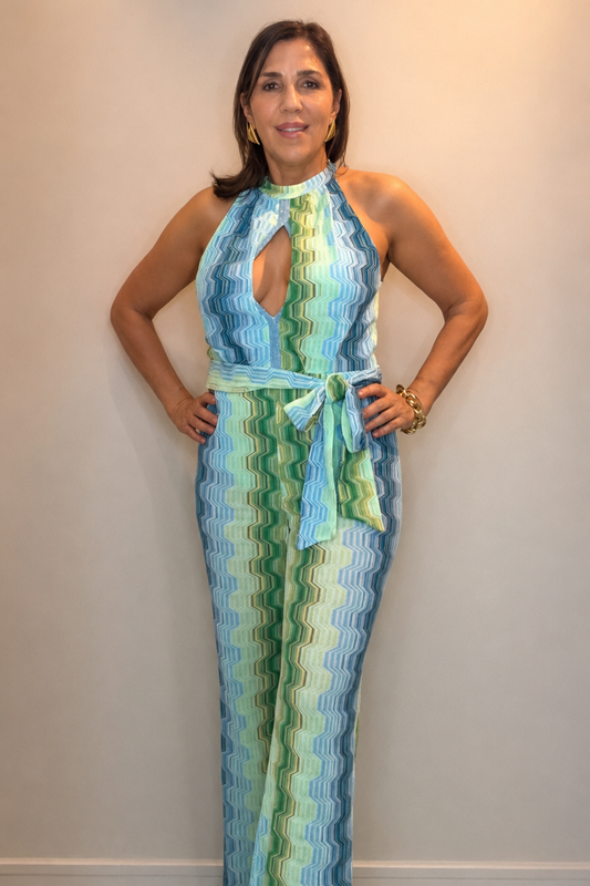 Woman wearing a green and blue wave print halter jumpsuit with waist tie detail and elegant wide-leg silhouette.