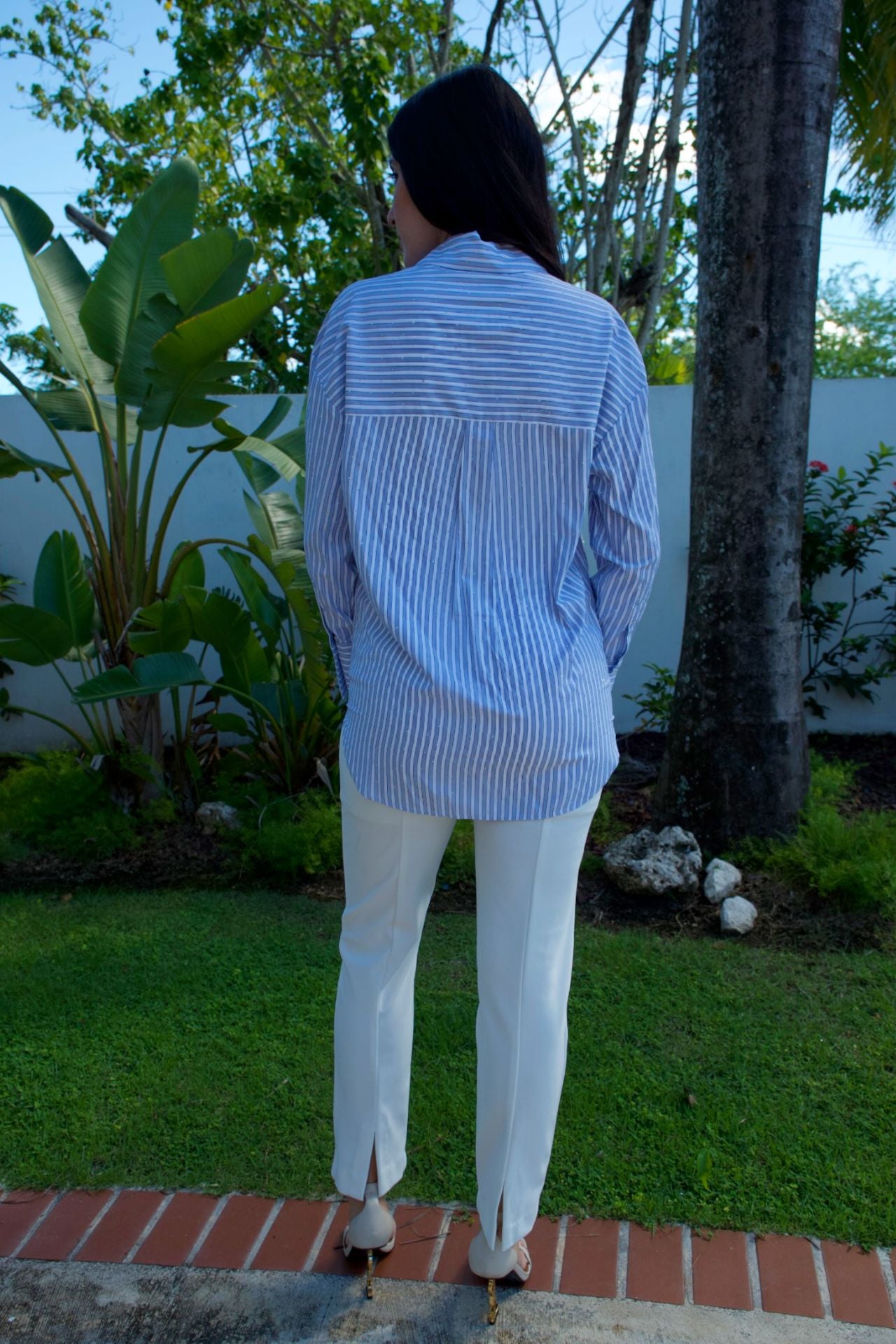 Model wearing light blue striped blouse with shimmer accents and white pants — casual chic look Elegance Boutique