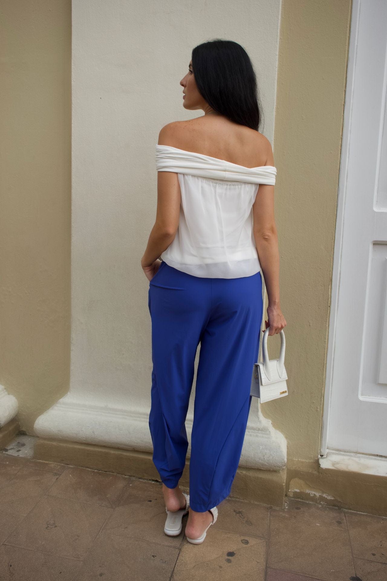 Woman wearing ivory off-shoulder chiffon top with elastic hem, paired with cobalt blue baggy pants.