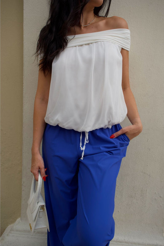 Woman wearing ivory off-shoulder chiffon top with elastic hem, paired with cobalt blue baggy pants.