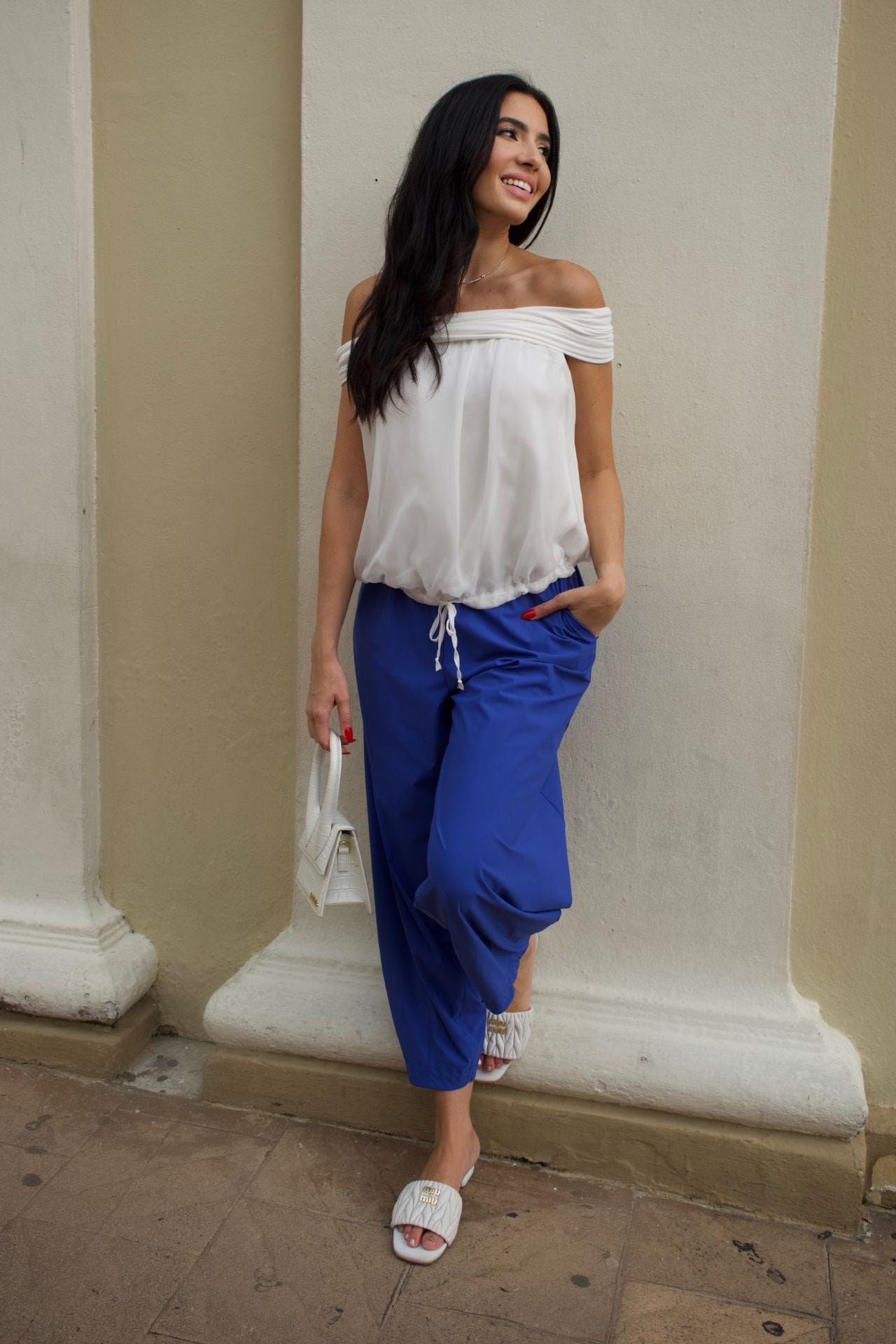 Woman wearing ivory off-shoulder chiffon top with elastic hem, paired with cobalt blue baggy pants.