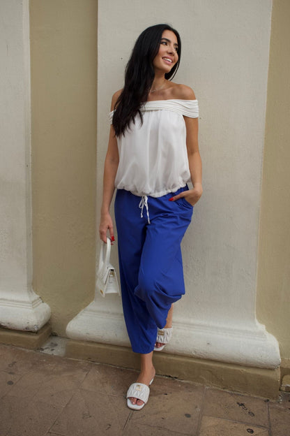 Woman wearing ivory off-shoulder chiffon top with elastic hem, paired with cobalt blue baggy pants.