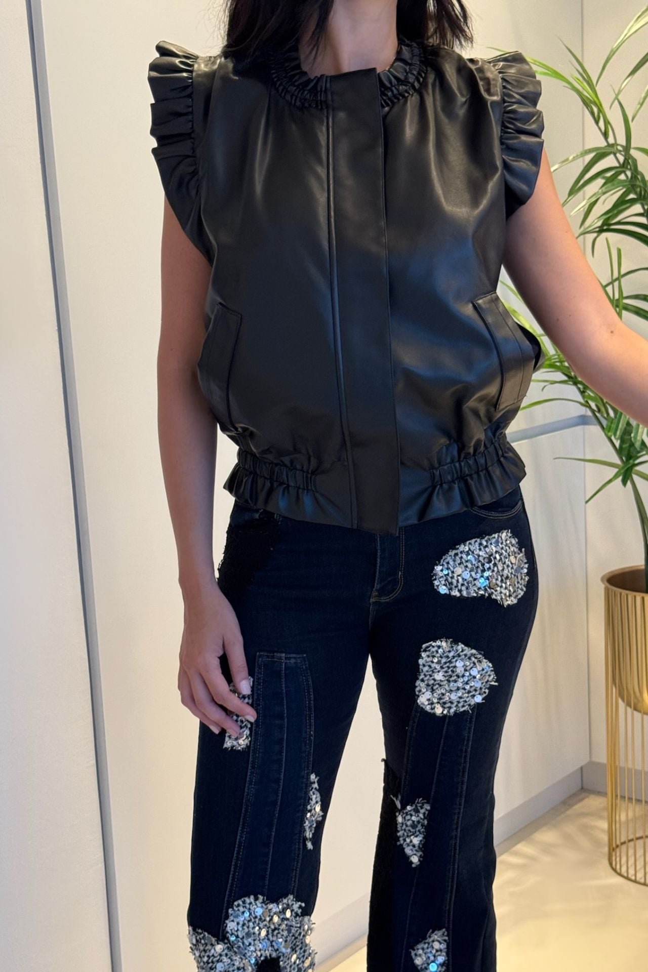 Black pleather vest with ruffle-trim shoulders and an elasticized hem.