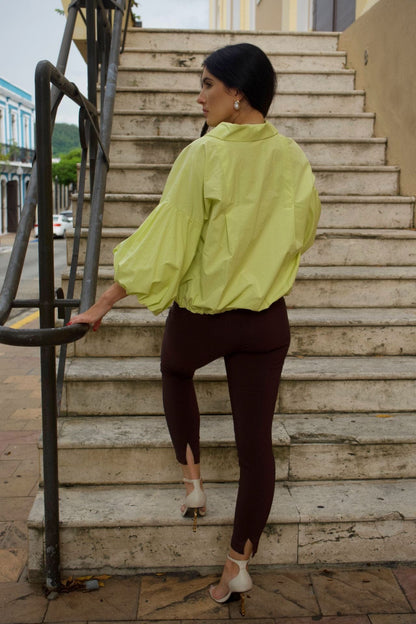 Back view of a woman wearing lime green crop jacket with puff sleeves and white buttons, standing on stairs.
