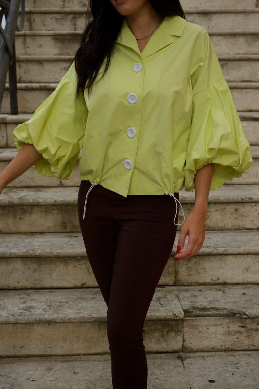 Woman wearing lime green crop jacket with puff sleeves and white buttons, standing on stairs.