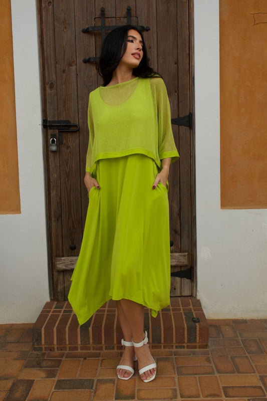 Woman wearing a lime green sleeveless jersey dress with a mesh overlay, standing in front of a rustic wooden door.

