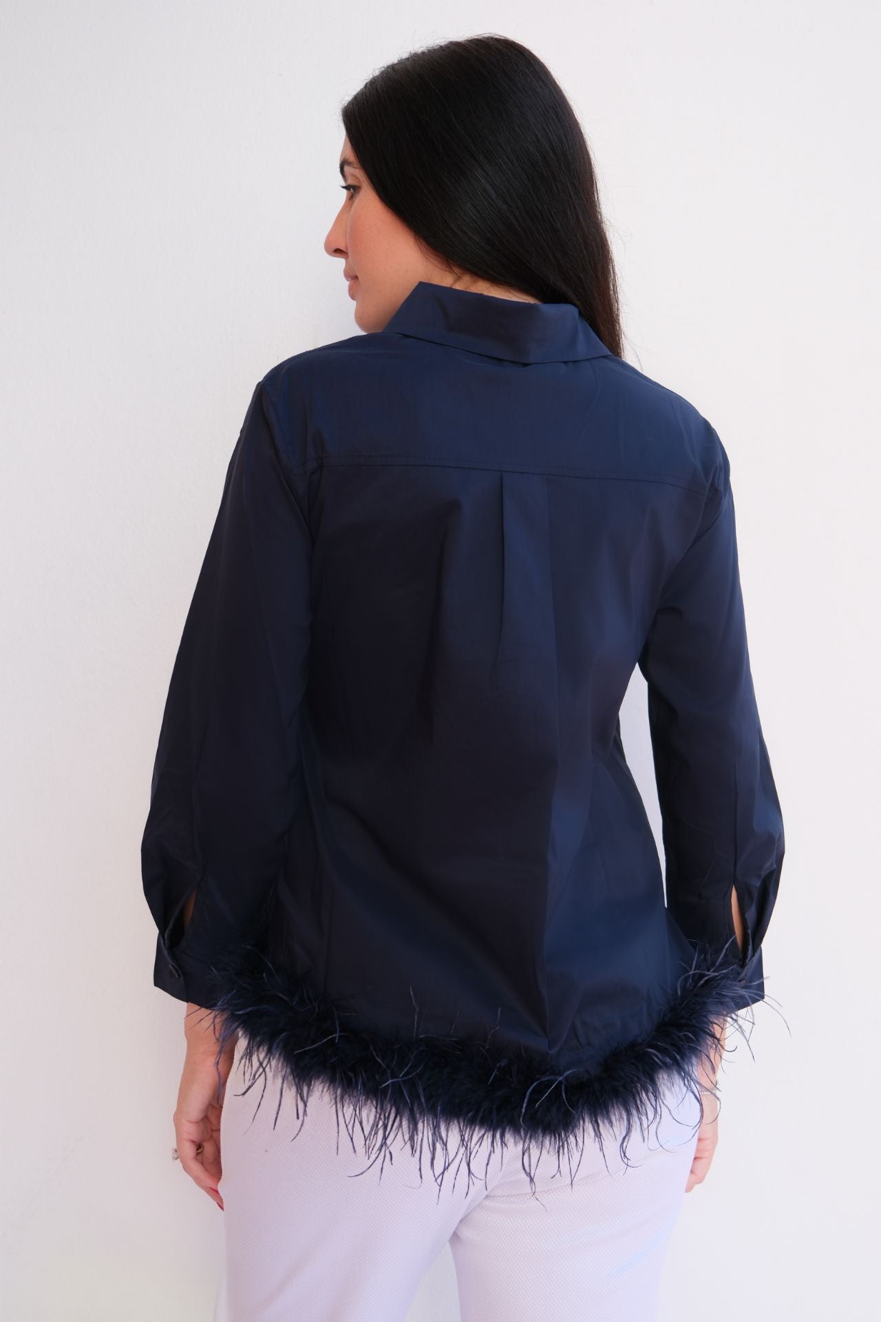 Woman wearing a navy satin button-down blouse with feather hem trim styled with light trousers for an elegant day-to-night look.