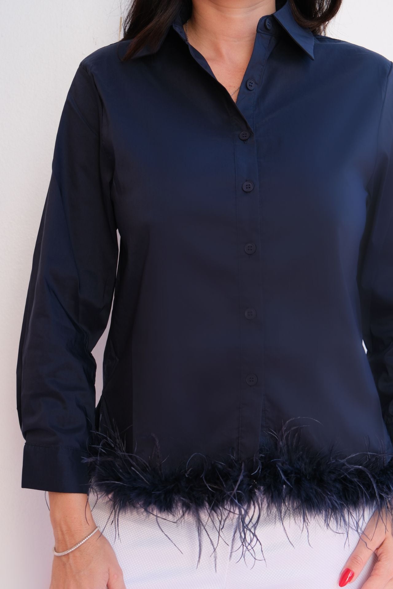 Woman wearing a navy satin button-down blouse with feather hem trim styled with light trousers for an elegant day-to-night look.
