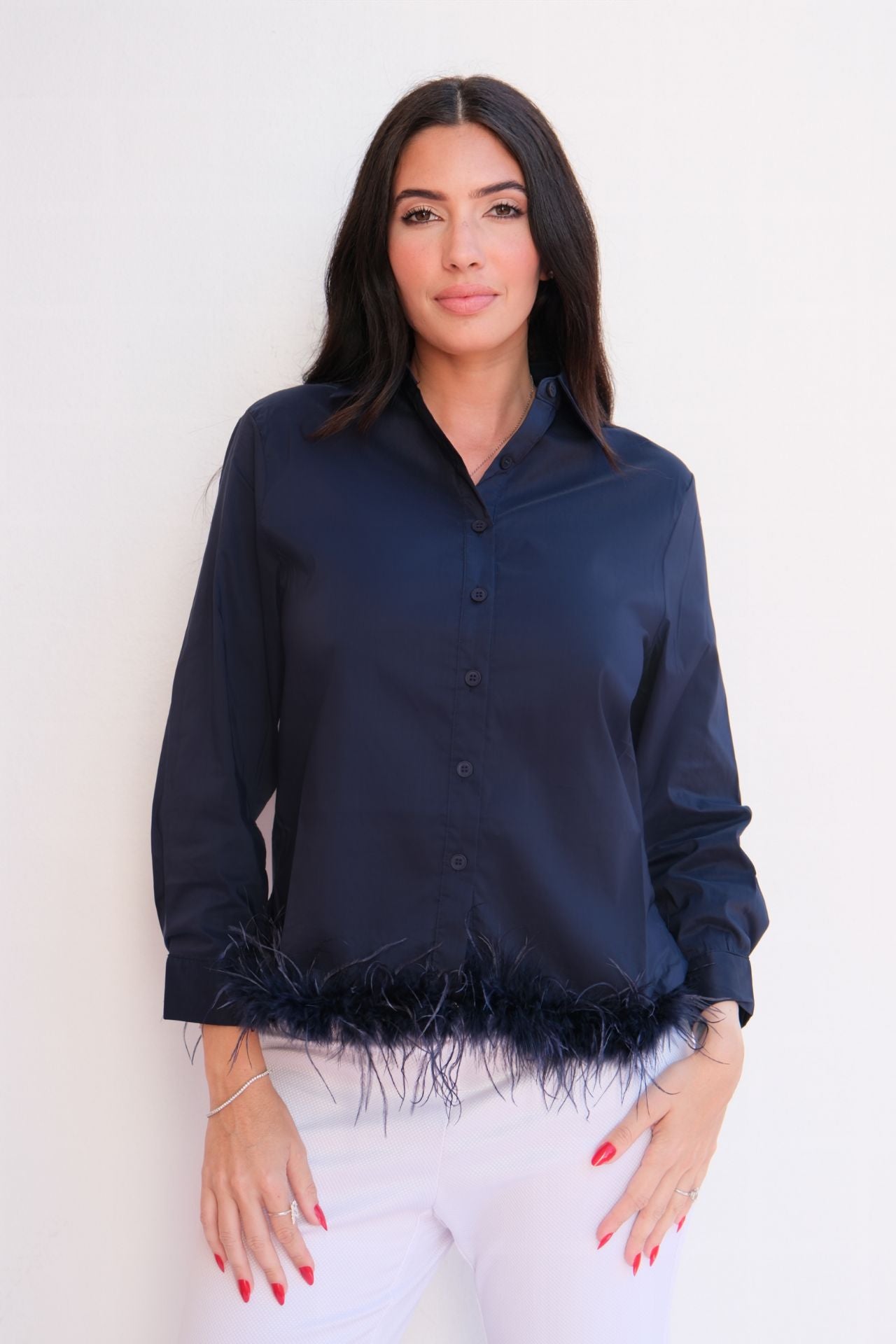 Woman wearing a navy satin button-down blouse with feather hem trim styled with light trousers for an elegant day-to-night look.