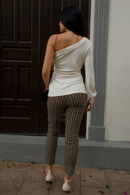 Back view of a woman wearing a cream one-shoulder blouse with long sleeve and tie-front detail, paired with printed pants.