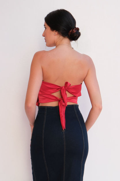Woman wearing a red strapless top with a bow detail and a dark denim pencil skirt