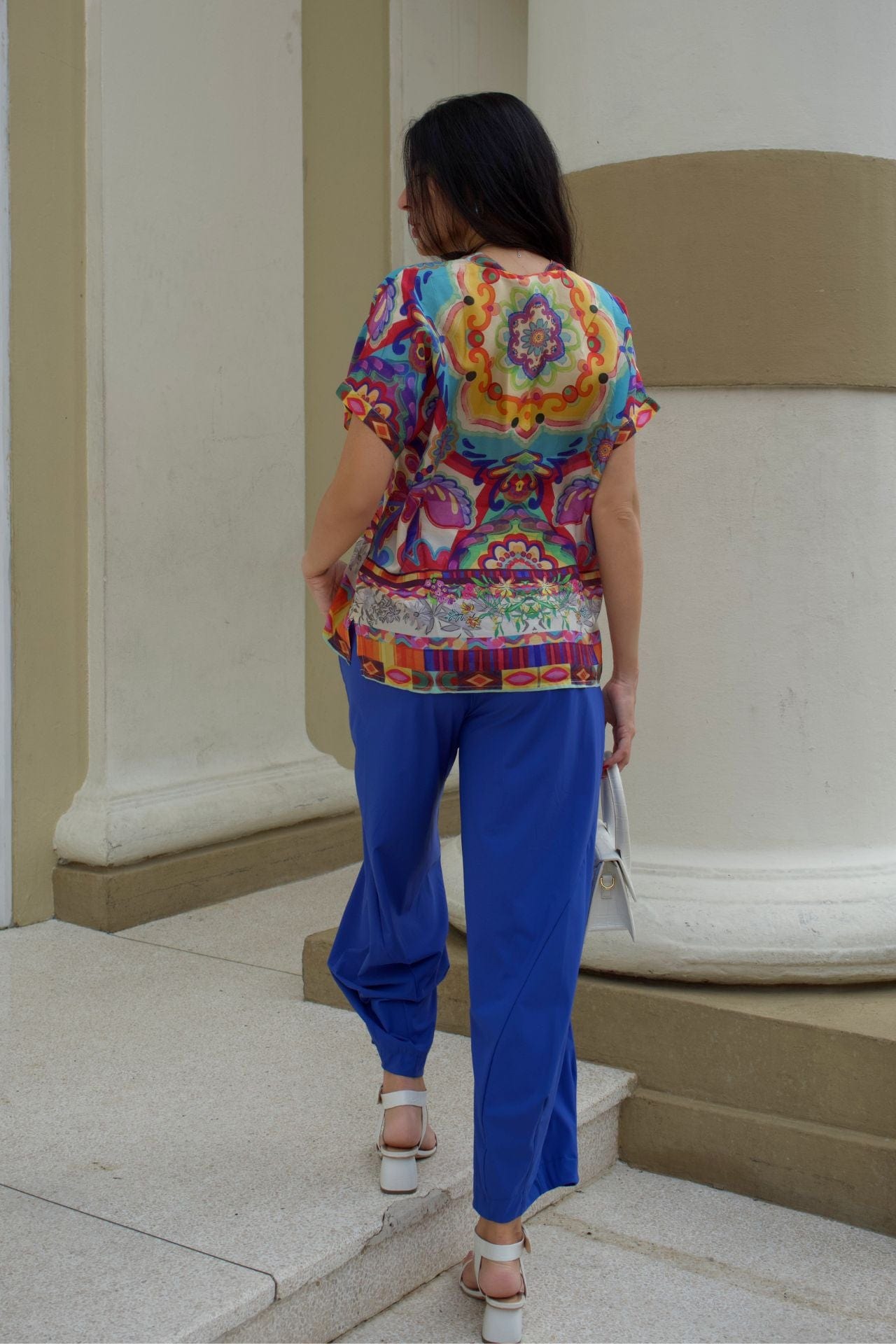 Back view of a woman wearing a colorful top and baggy royal blue pants. 