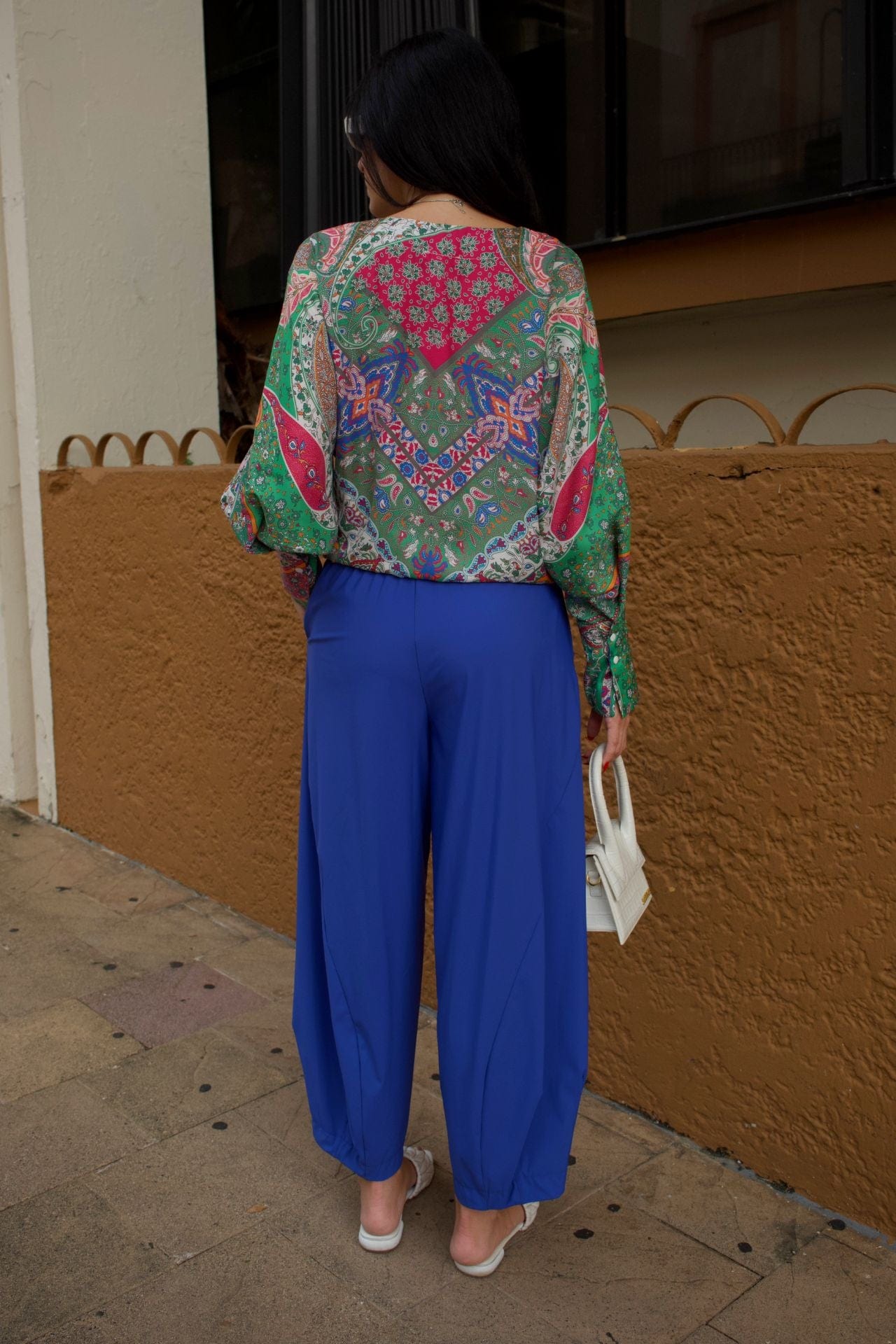 Back view of a women wearing a colorful patterned top and baggy royal blue pants. 