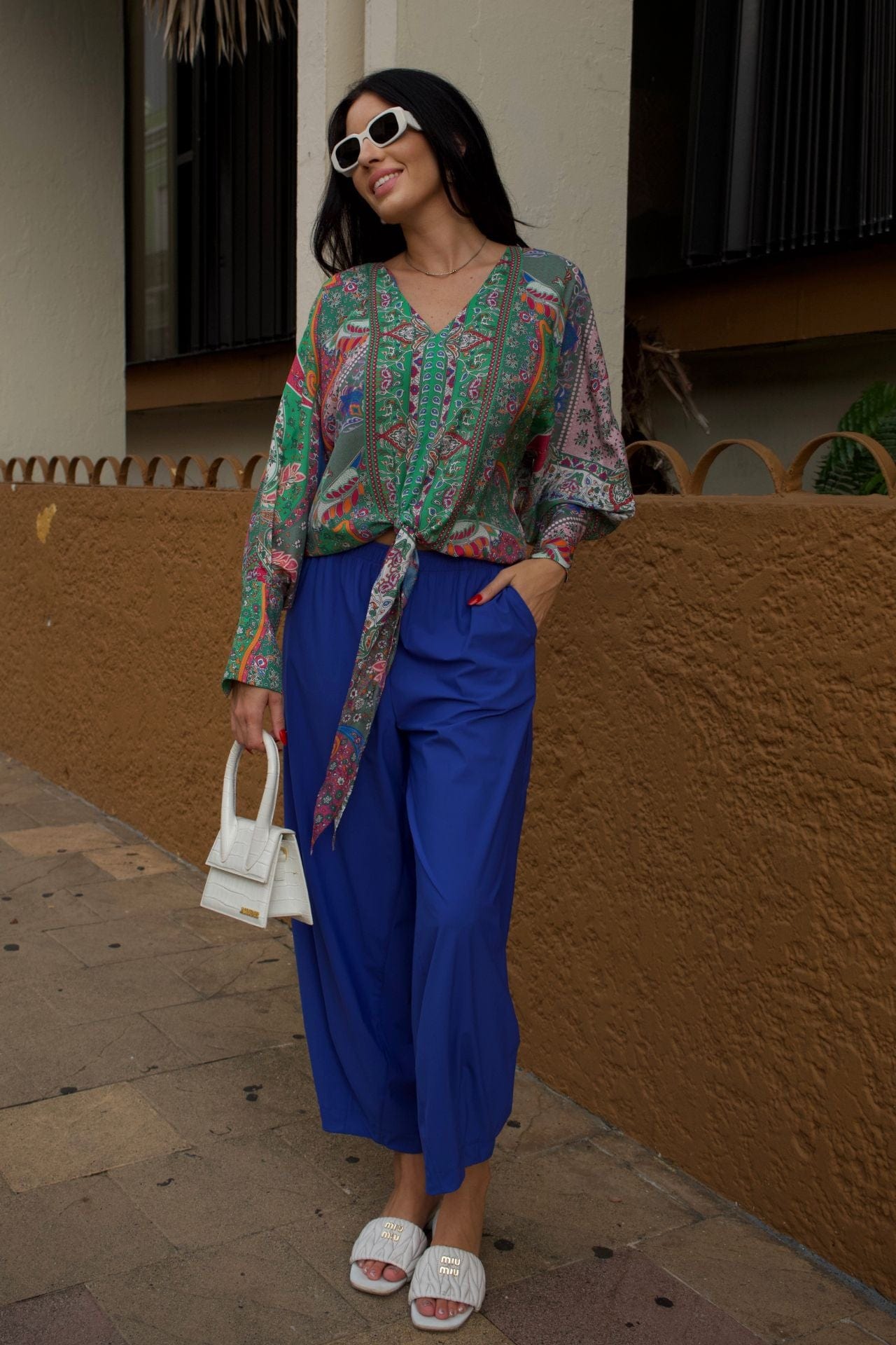 Woman wearing a colorful patterned blouse and  baggy royal blue pants.